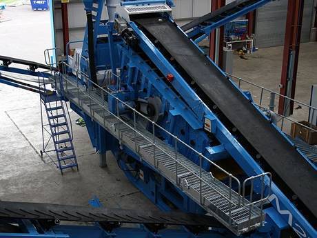 Steel grating walkways are on both sides of conveyor belt.