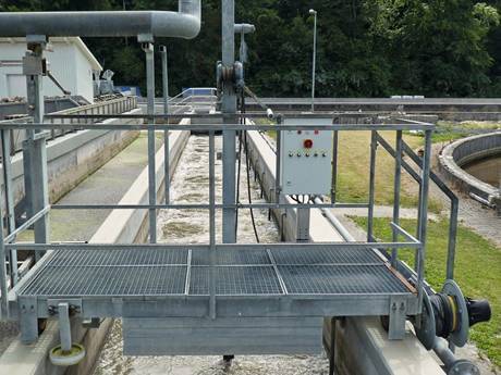 A steel grating walkway with handrails crossing gutter.