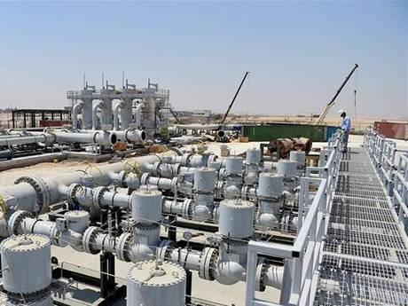 This is a big outdoor power station that a people stand on the steel grating walkway.